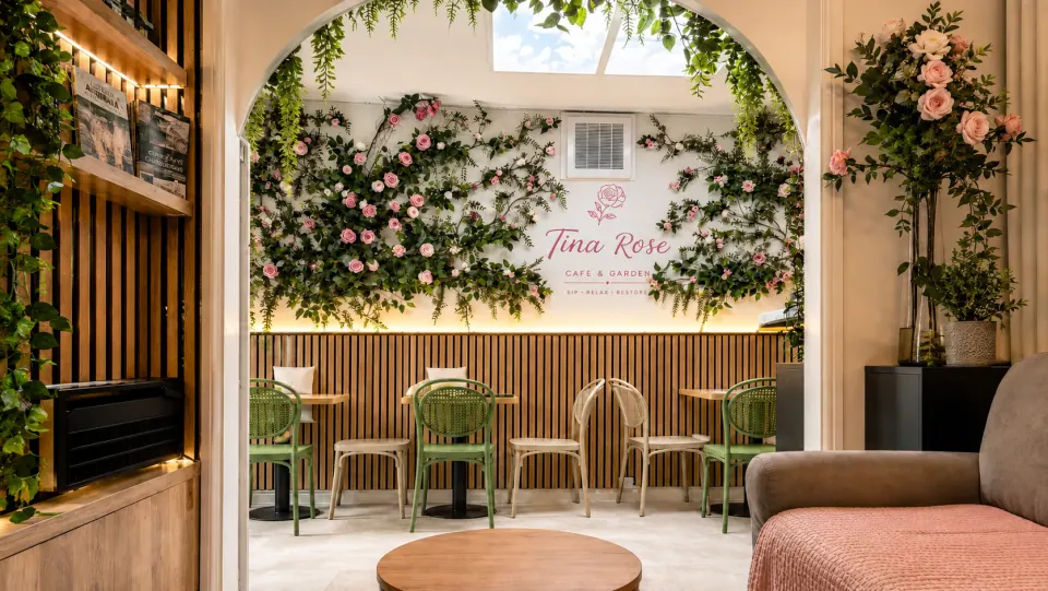 A flower-covered arch frames Tina Rose Cafe and Garden's pink signage and welcoming seating