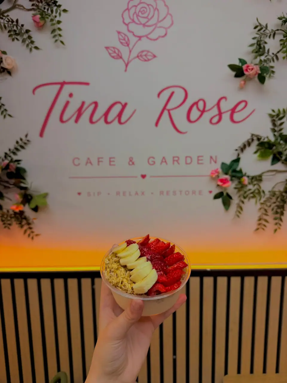 A fresh fruit and granola bowl in front of Tina Rose's floral Cafe and Garden sign